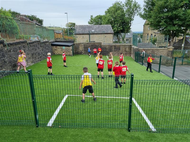 children in red and yellow vests play football on the new pitch