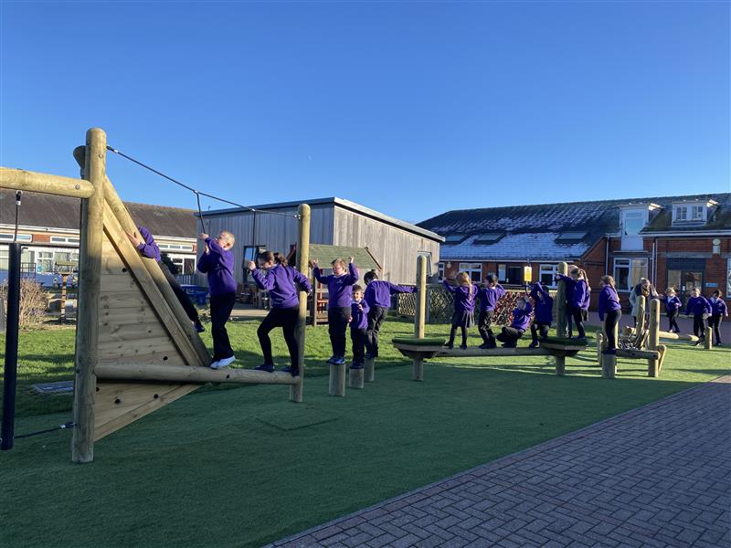 A whole class climbing across the trim trail in their school playground
