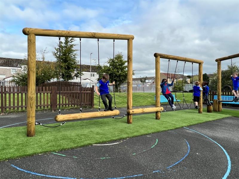 A group of young children playing on the trim trail in the school playground