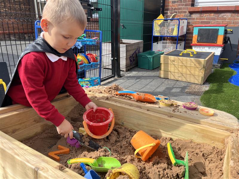A young boy playing in the sandbox in the playground