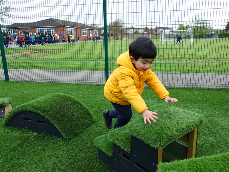 a young boy climbing on up the artificial grass topped movable block