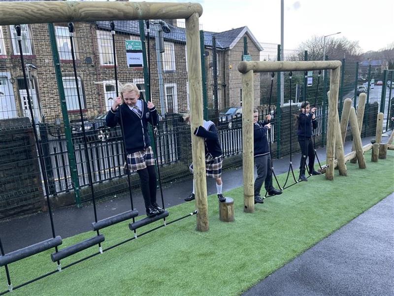 A group of children climbing across the trim trail in their playground