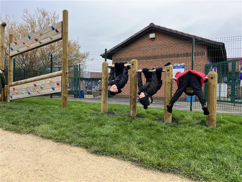3 children rolling over the bars in their playground setting