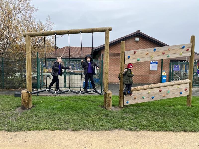 A couple of children climbing across the trim trail in their primary school playground and a young boy is running across