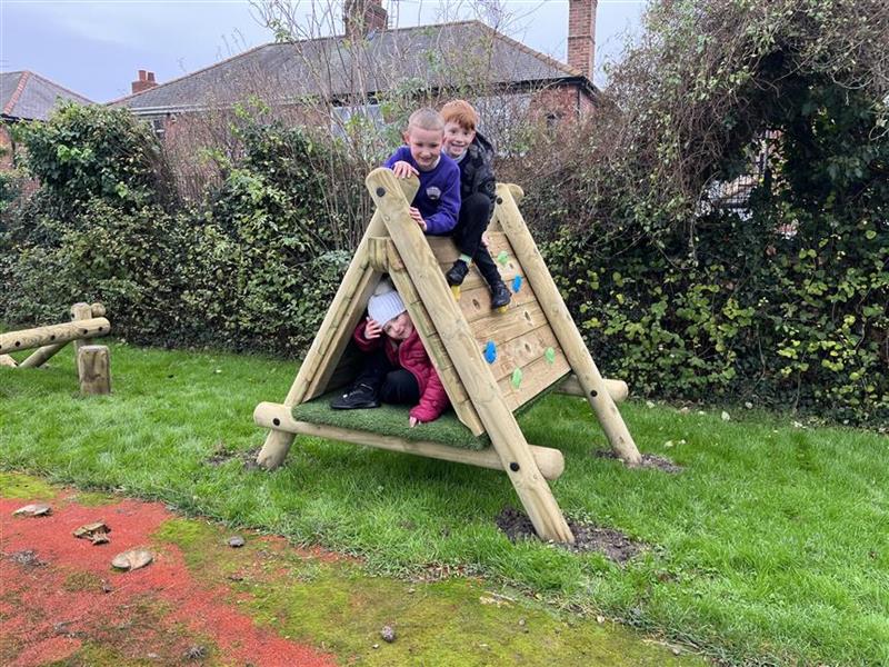 two children climbing over the triangle climbing frame in their playground setting