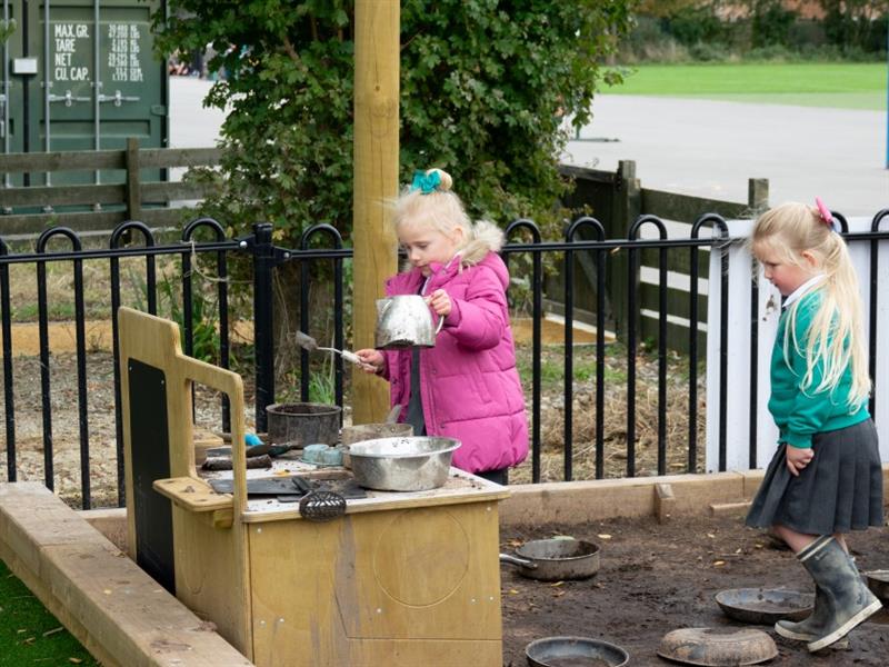 two little girls stand in the messy play mud space and play with the mud kitchens