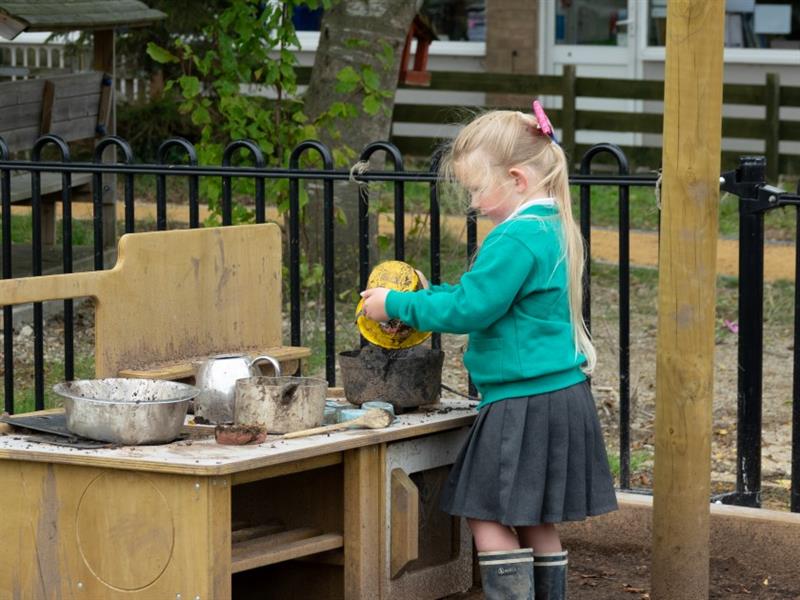 a little girl stands at the mud kitchen and mixes and makes with the mud