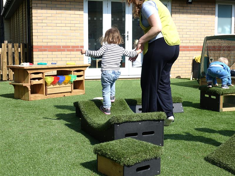 A teacher helping a nursery child to climb over the block in their playground 