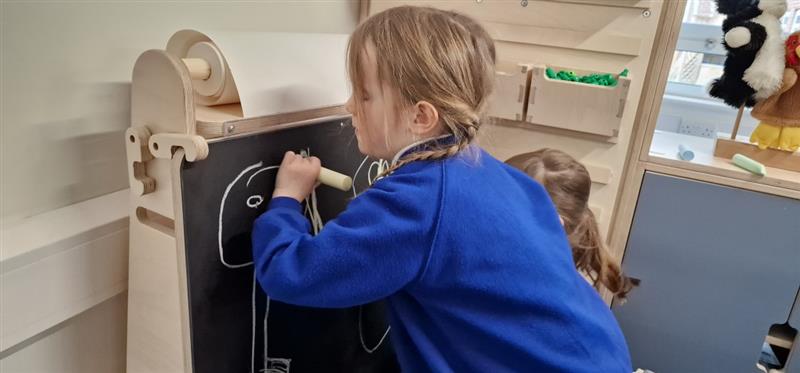 a little girl builds her fine motor skills by writing on the chalkboard
