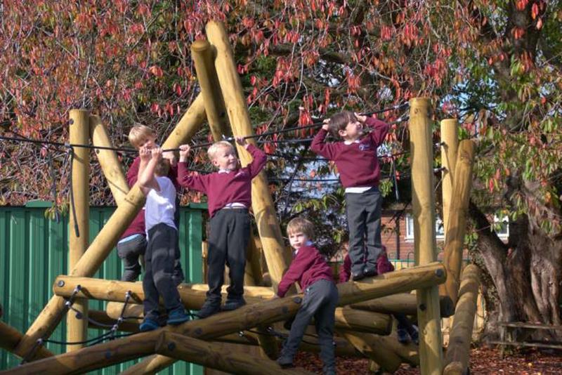 5 young boys climbing and swinging on the climbing frame in their playground 