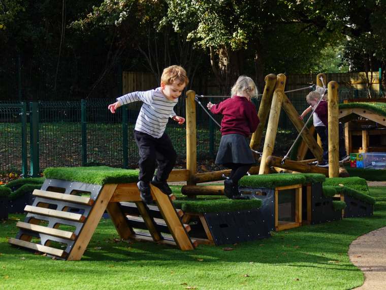 A young boy jumping from one of the blocks in his playground 
