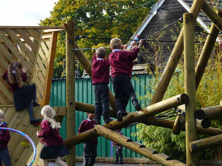 A class of children playing on the ropes of the climbing frame in their new playground development