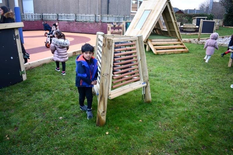 children play on the new playground, and a child poses in front of the musical triad