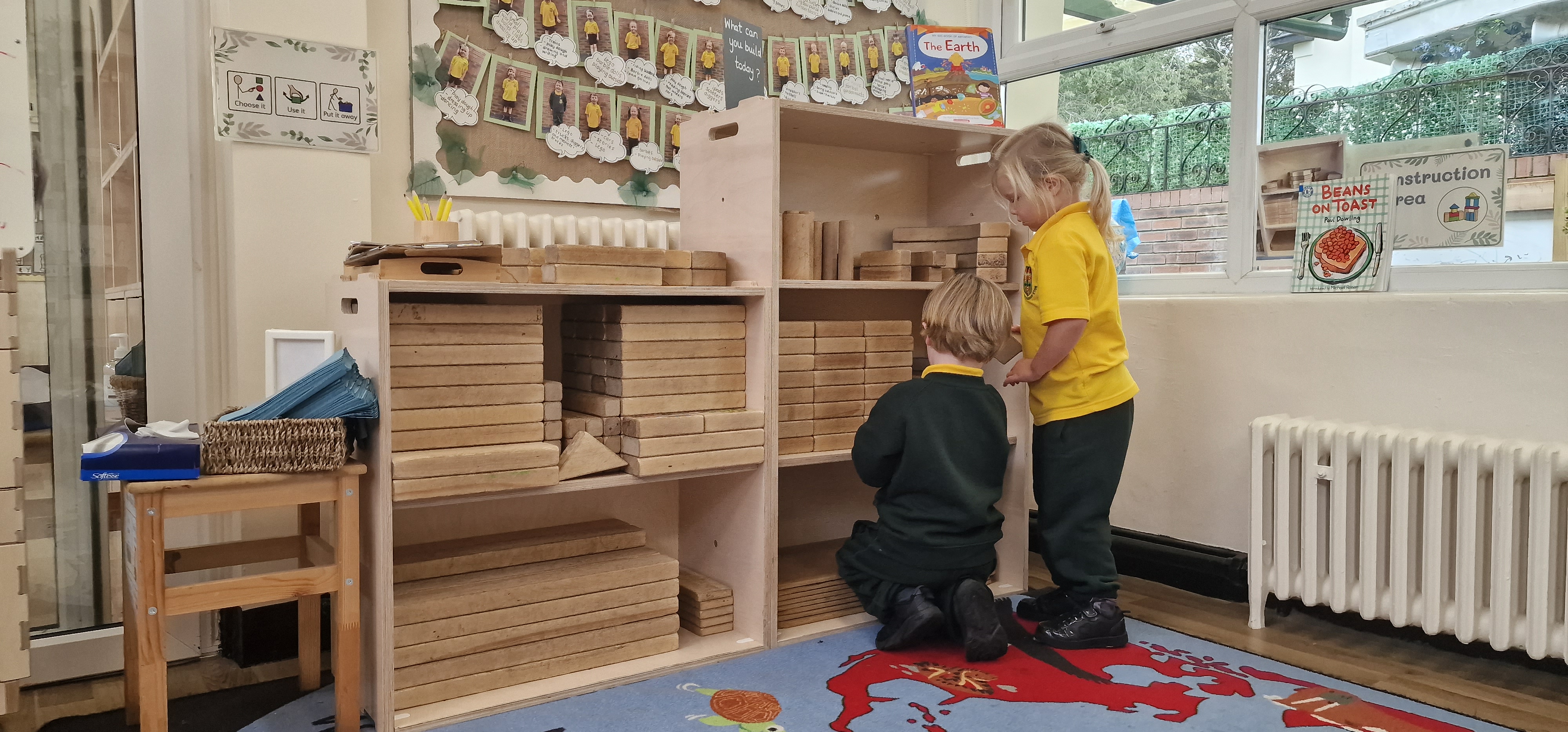 An image showing two children looking at the storage unit with shelves we provided. This storage unit is holding wooden blocks.