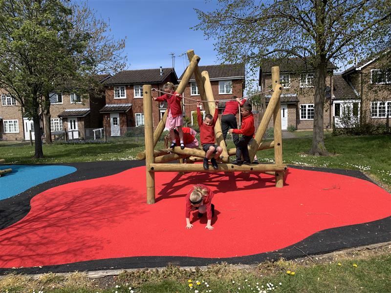 five children playing on climbing frame, which is on red wet pour surrounded by black wetpour