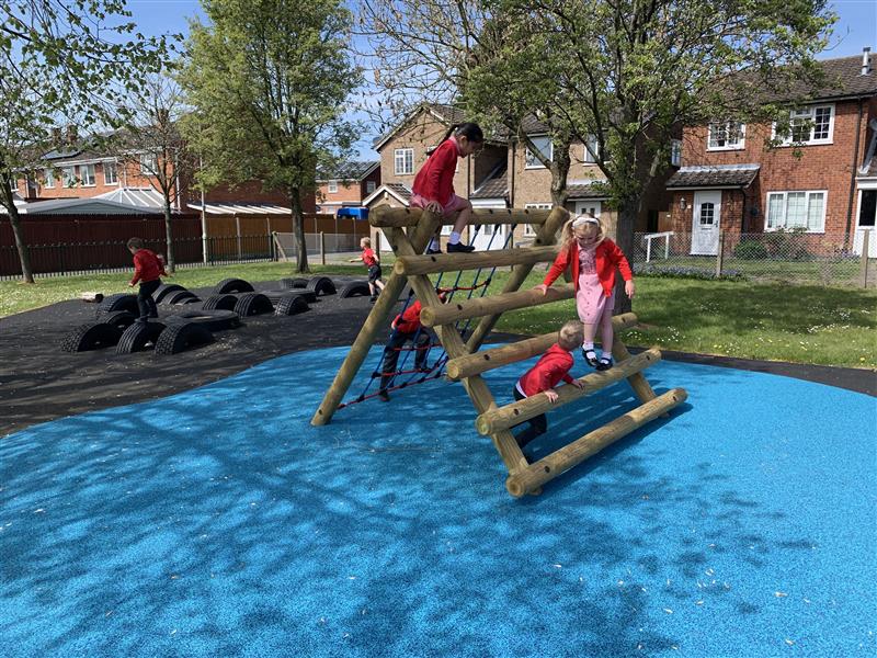 four children playing on climbing frame which is on top of blue wetpour