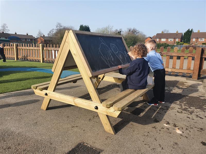 Two children sat at an easel table drawing on the chalkboard