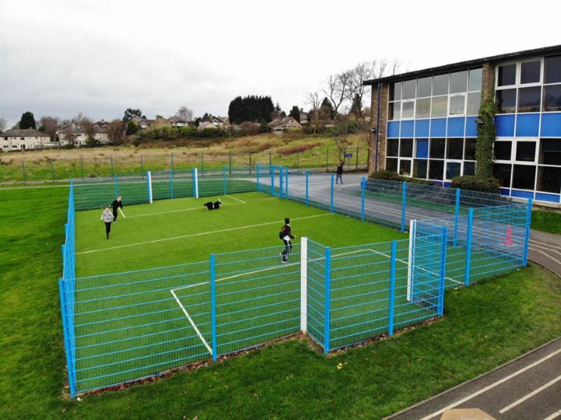 5 children playing football on a 20m x 12m muga pitch with blue sport fencing, recessed goal ends and bright green artificial grass