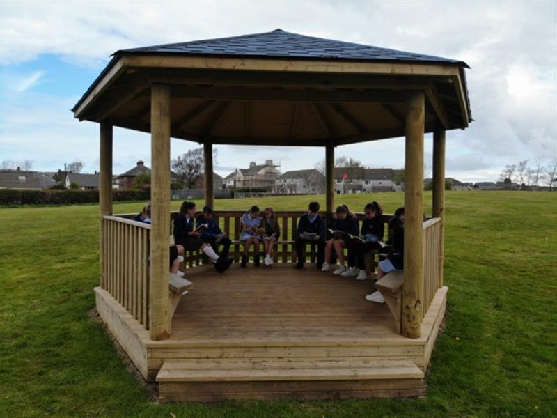 A class of children sat on the internal benches of an outdoor classroom reading books