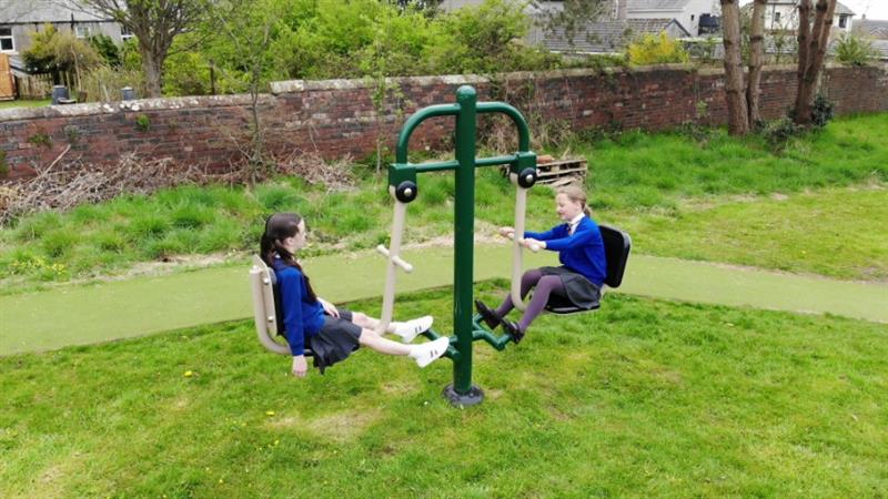 2 children exercising on a seated leg press installed on their school playground