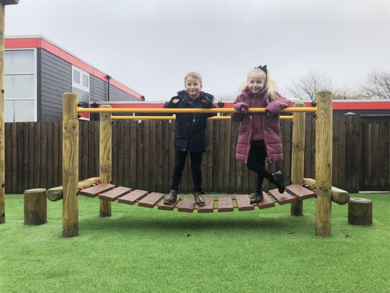 Two children stood on a timber clatter bridge holding onto bright yellow bars