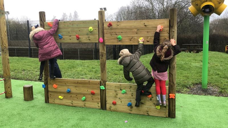Three children moving across a timber climbing wall gripping the multi coloured climbing wall. 