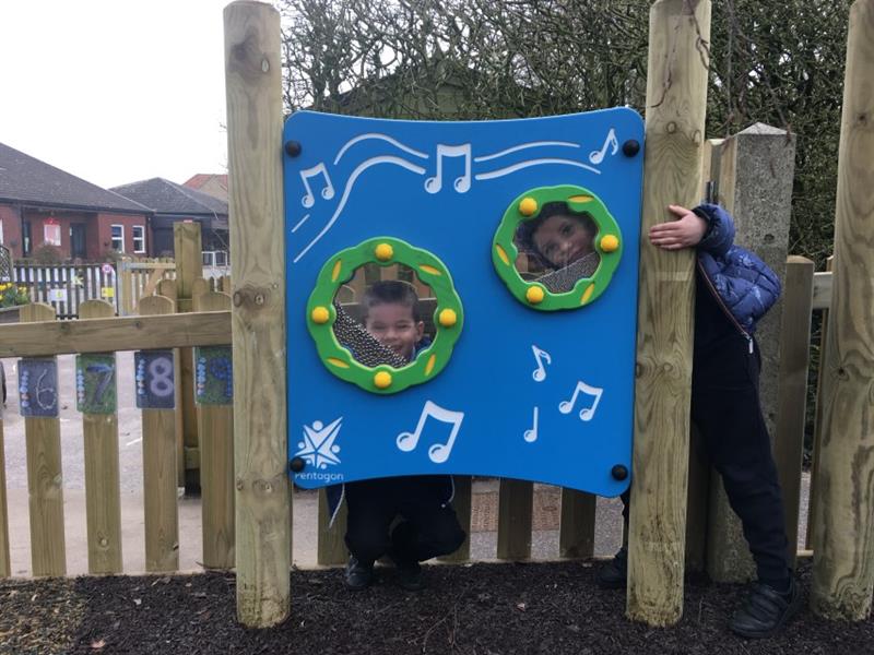 Two children stood behind the blue shaker panel post showing their faces through the transparent circles, installed in front of the timber fence. 
