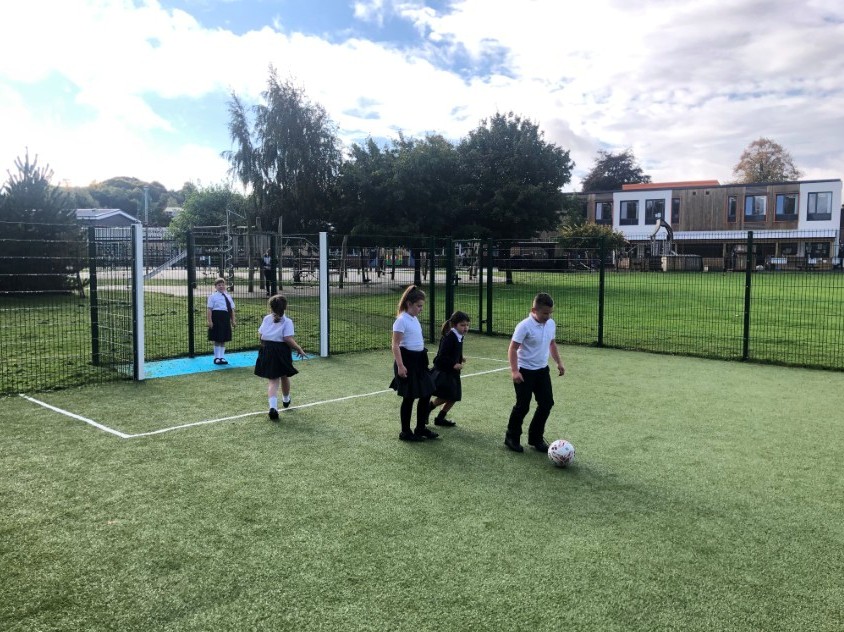 Children playing football on a muga pitch that has been installed onto a school field