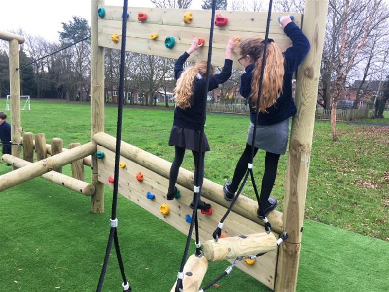 Two children in black uniforms traversing across an inclined climbing wall installed on the school playground