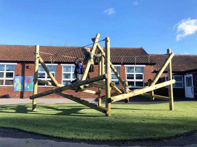 two children climbing on top of pentagon play's tryfan climbing frame. One child is hanging on the ropes and the other is balancing on the beams
