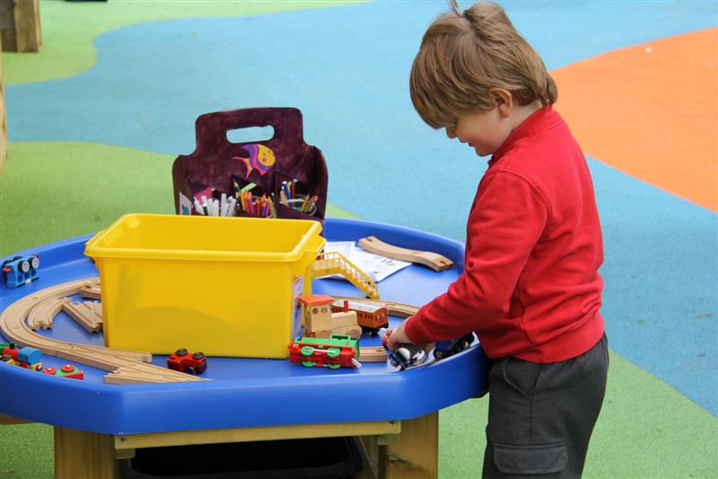 a child stands over a tuff spot table and plays with train track items