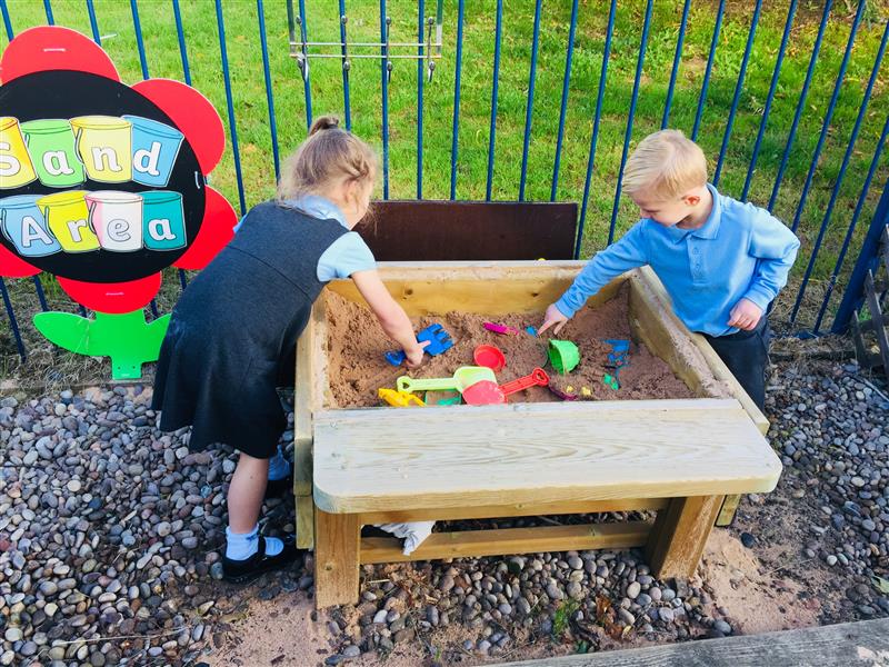 Two children playing in a sand table placed on stones with loose play resources