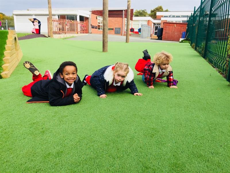 three little girls in red and white uniform with winter coats on lie on the green artificial grass smiling at the camera in front of them