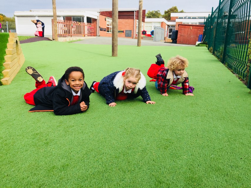 Three girls are lay on top of an artificial grass surface and are smiling towards the camera.