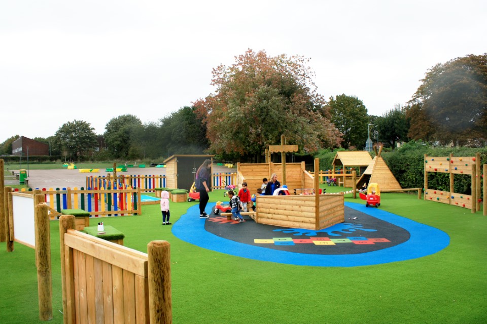 A big playground with a variety of different safety surfacing on it. With some play turf and wetpour, a lot of different designs are displayed, making the playground very vibrant. In the centre, a play ship can be seen with children and teachers playing.