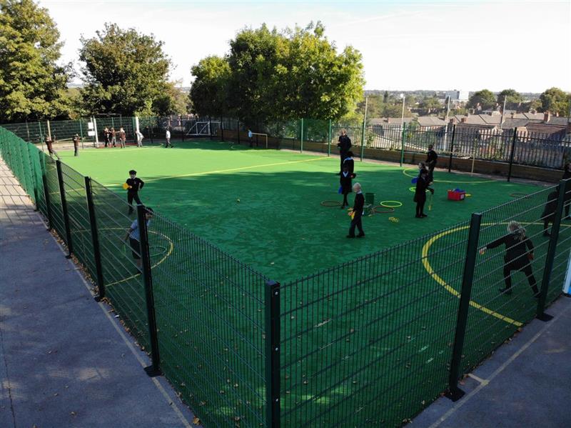 a photo of the green muga in the bright playground with children playing football on the new pitch
