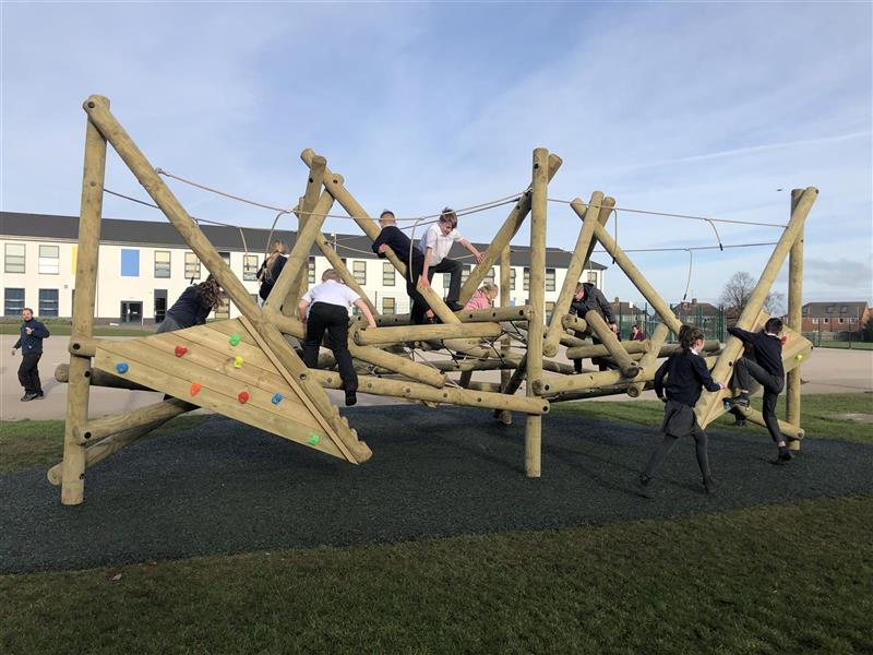 9 children are playing on a huge climbing frame with a climbing wall, the climbing frame has been installed onto the school playground in front of the white school building. 