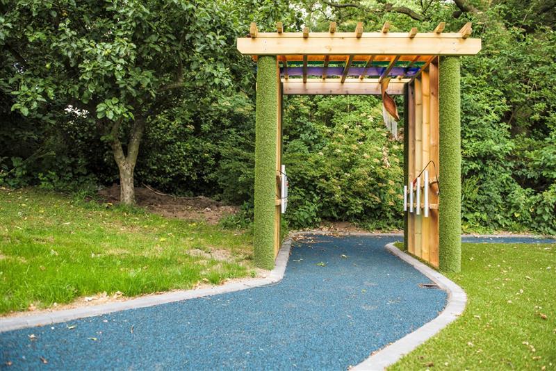 A side view of our sensory tunnel, the two pillars at the front are coated in artificial grass, a blue wetpour path goes through the middle.