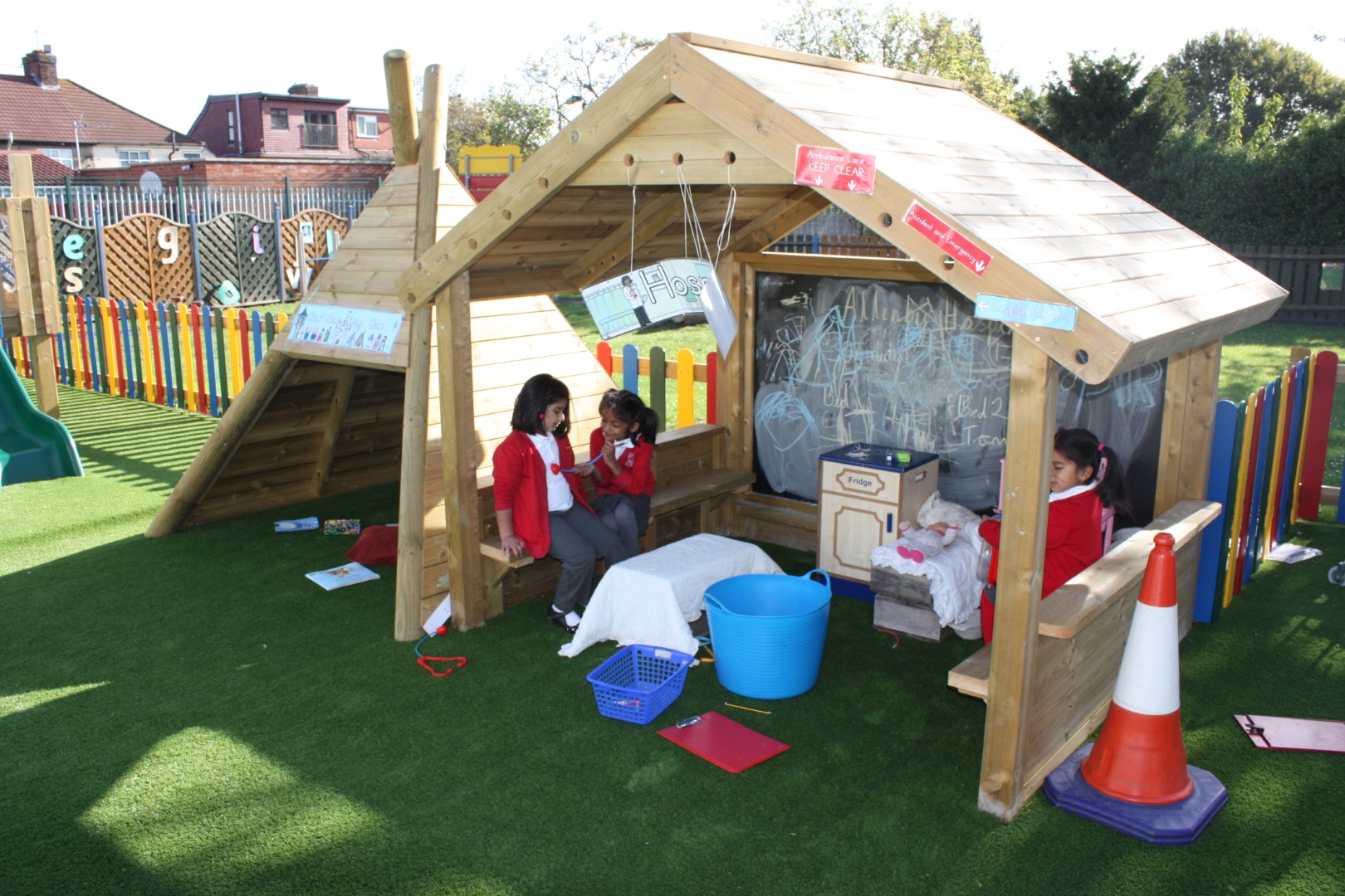 A picture of an outdoor playhouse where three children carrying out creative play activities whilst the sun is shining