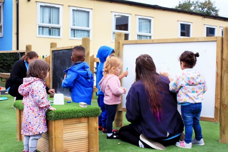 children stand in raincoats outdoors as they look at a whiteboard