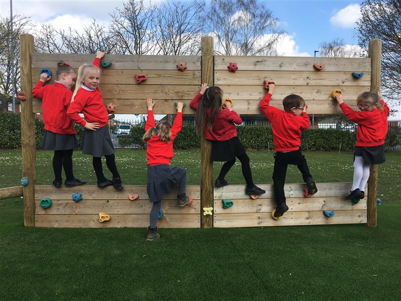 children in red school uniform cross the climbing wall and pose for a picture 