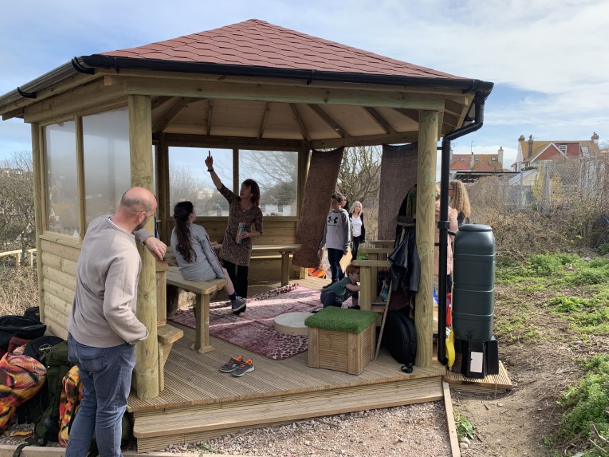 A group of teachers and children are decorating the inside of their classroom gazebo.