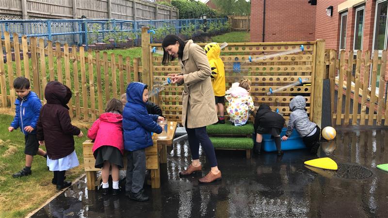 children in school uniform and raincoats play outdoors with the water wall product