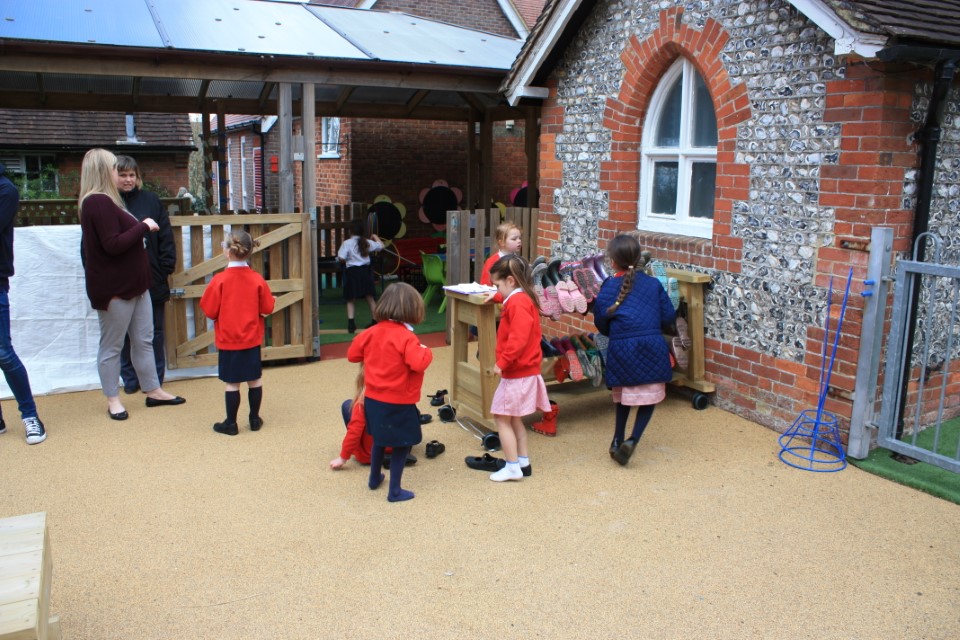 A teacher is supervising her students as they are taking off their shoes and putting them on the storage unit