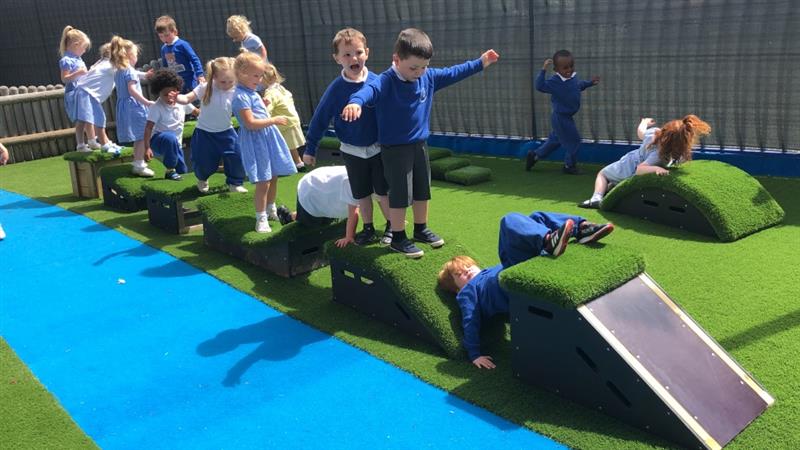  15 children are playing on get set, go! blocks that have been placed onto artificial grass next to bright blue safeturf surfacing. 