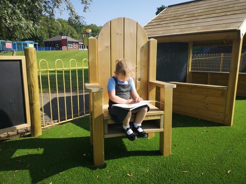 a little girl sits on a freestanding wooden storytelling chair and reads a book