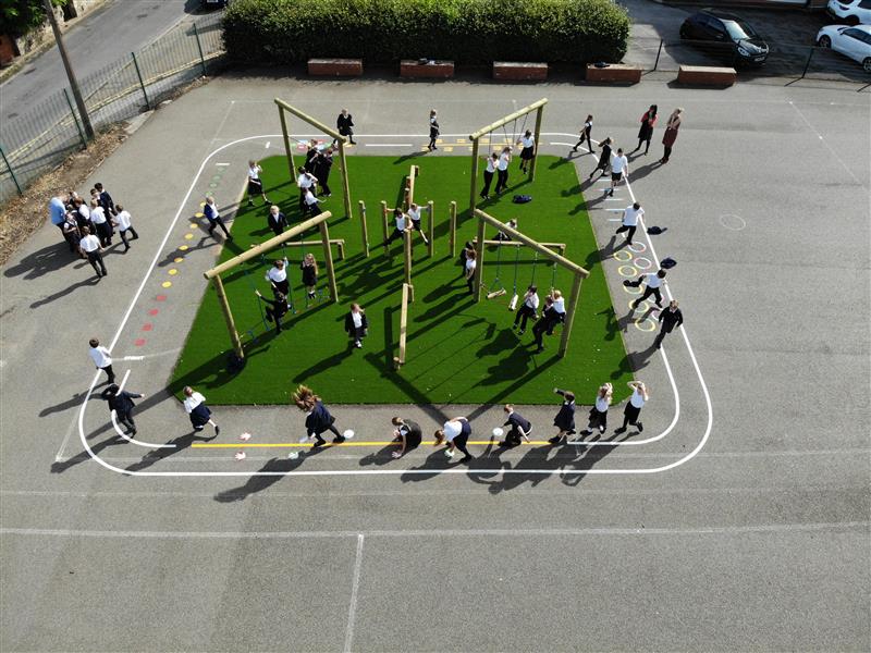 A class of children playing on an adventure climbing frame that has been installed onto artificial grass with playground markings around the climbing frame. 