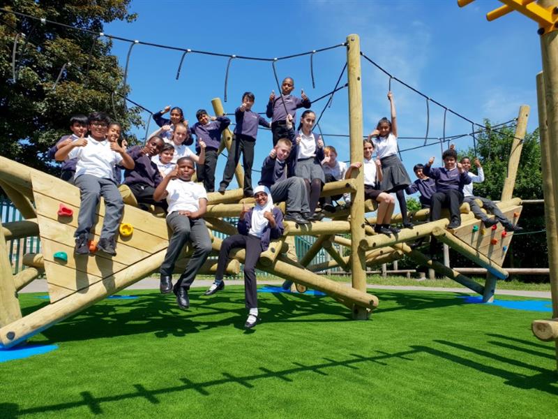 children climb on the timber climbing frame and pose for a picture with artificial grass surfacing beneath