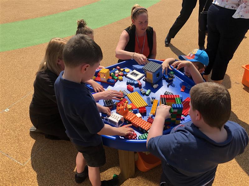 children play with the tuff spot table with legos as their teacher supervises them