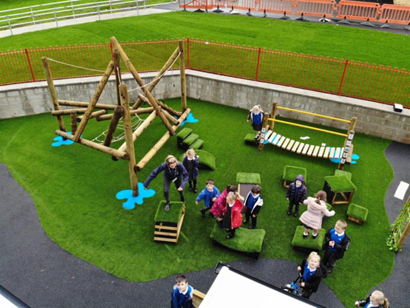 children run around on the artificial grass urfacing and play on the timber climbing frame, the get set go blocks and the wobbly bridge